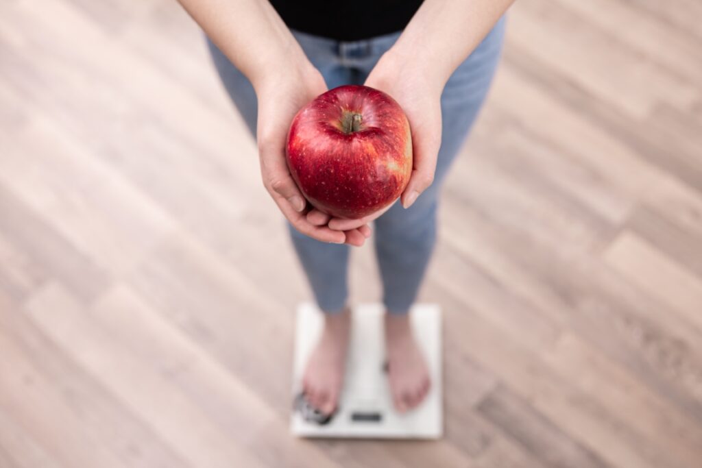 Zena drži jabuku u krukama dok stoji na tjelesnu vagu