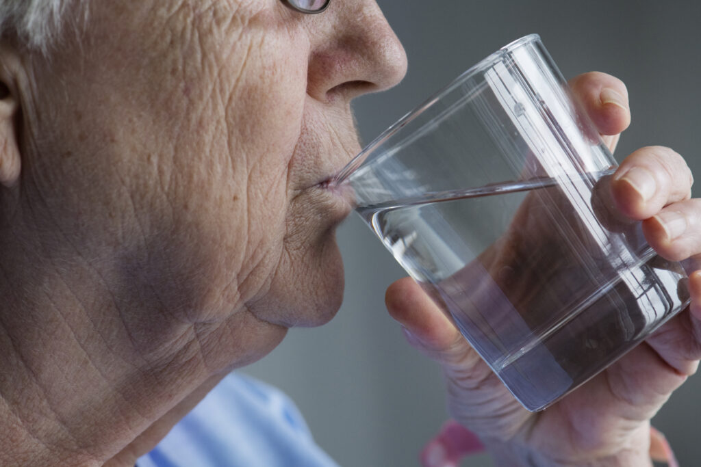 Starija žena pije čašu vode (iz profila)